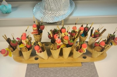 Cônes en gaufrette garnis de bonbons colorés et de biscuits, disposés sur un présentoir en bois.