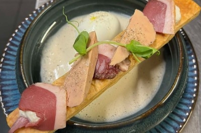 Assiette contenant une soupe crémeuse, garnie d'une pâte feuilletée avec foie gras, magret fumé et pousses de pois.