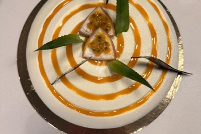 Gâteau rond décoré de spirales orange, morceaux de fruit de la passion et feuilles vertes sur le dessus.