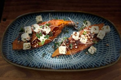 Patate douce rôtie garnie de fromage, graines, micro-pousses et herbes, servie sur une assiette bleue.