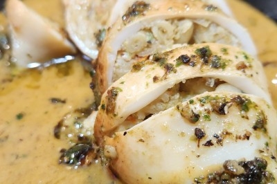 Calamar farci servi dans une sauce crémeuse aux herbes, présenté dans une assiette noire.