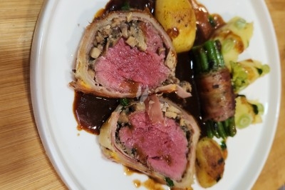 Plat de bœuf Wellington tranché, accompagné de pommes de terre, haricots verts enroulés de lard et sauce brune.