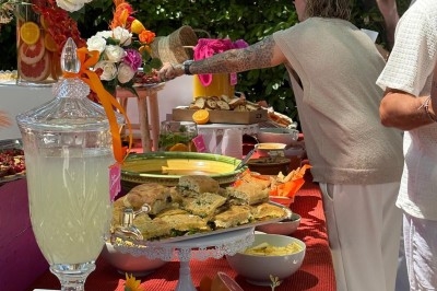 Buffet en plein air avec boissons, plats variés, fleurs colorées et convives se servant.