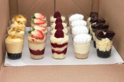 Assortiment de verrines sucrées variées avec fruits, mousse et chocolat, disposées dans une boîte en carton.