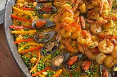 Grande poêle de paella garnie de crevettes, moules, légumes colorés et riz safrané, présentée sur une table en bois.