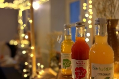 Bouteilles de jus artisanaux disposées sur un support en bois, éclairées par des guirlandes lumineuses dans un décor…
