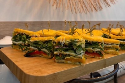 Assortiment de sandwichs végétariens colorés présentés sur une planche en bois, maintenus par des pics en bois.