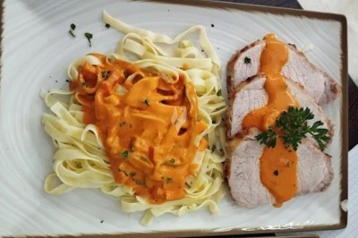 Assiette contenant des tagliatelles nappées de sauce tomate crémeuse et des tranches de rôti garnies de persil.