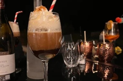 Verre de cocktail avec mousse et paille rouge et blanche, posé sur une table noire avec d'autres verres en arrière-plan.