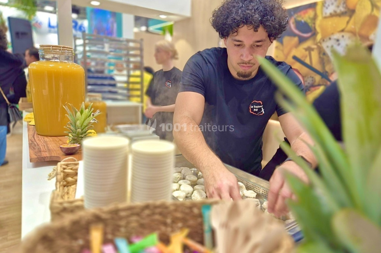 Un homme prépare des aliments sur un stand culinaire avec des boissons et des accessoires en arrière-plan.