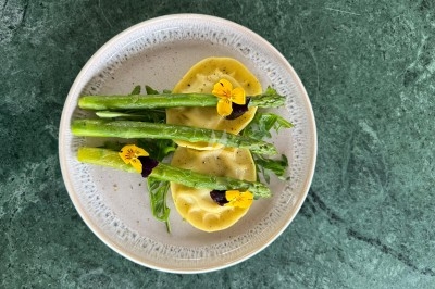 Assiette de raviolis garnis de roquette, asperges et fleurs comestibles, présentée sur une table en marbre vert.