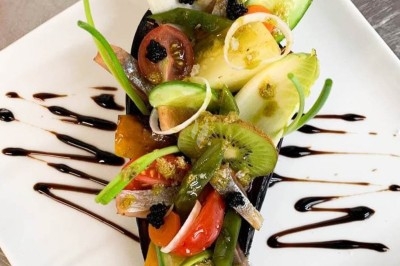 Assiette gastronomique composée de légumes frais, caviar végétal et sauce balsamique sur une présentation soignée.