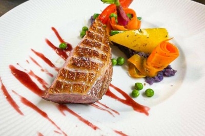 Assiette gastronomique avec magret de canard grillé, purée violette, légumes sculptés et sauce rouge décorative.