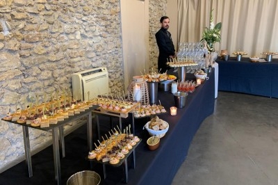 Buffet de réception avec amuse-bouches variés, verres et décor sobre dans une salle aux murs en pierre.