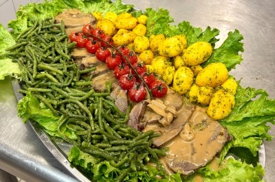 Plateau garni de rôti en sauce, haricots verts, pommes de terre persillées, tomates cerises et feuilles de salade.