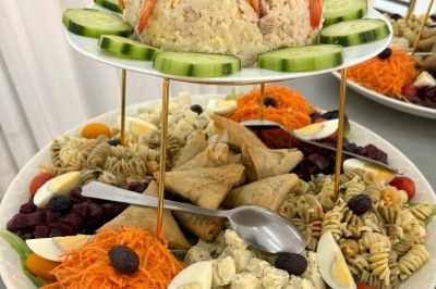 Assortiment de salades, samoussas et crevettes disposés sur un plateau avec décoration de légumes et œufs.