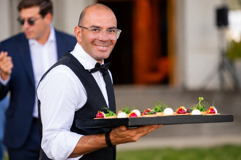 Serveur en costume présentant un plateau de petits fours sur canapés aux fruits rouges et herbes fraîches.